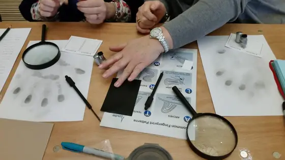 Hands examining fingerprint evidence with magnifying glasses