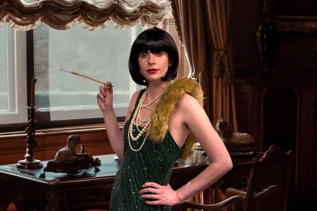An actor in a green 1920s flapper dress, holding a cigarette holder