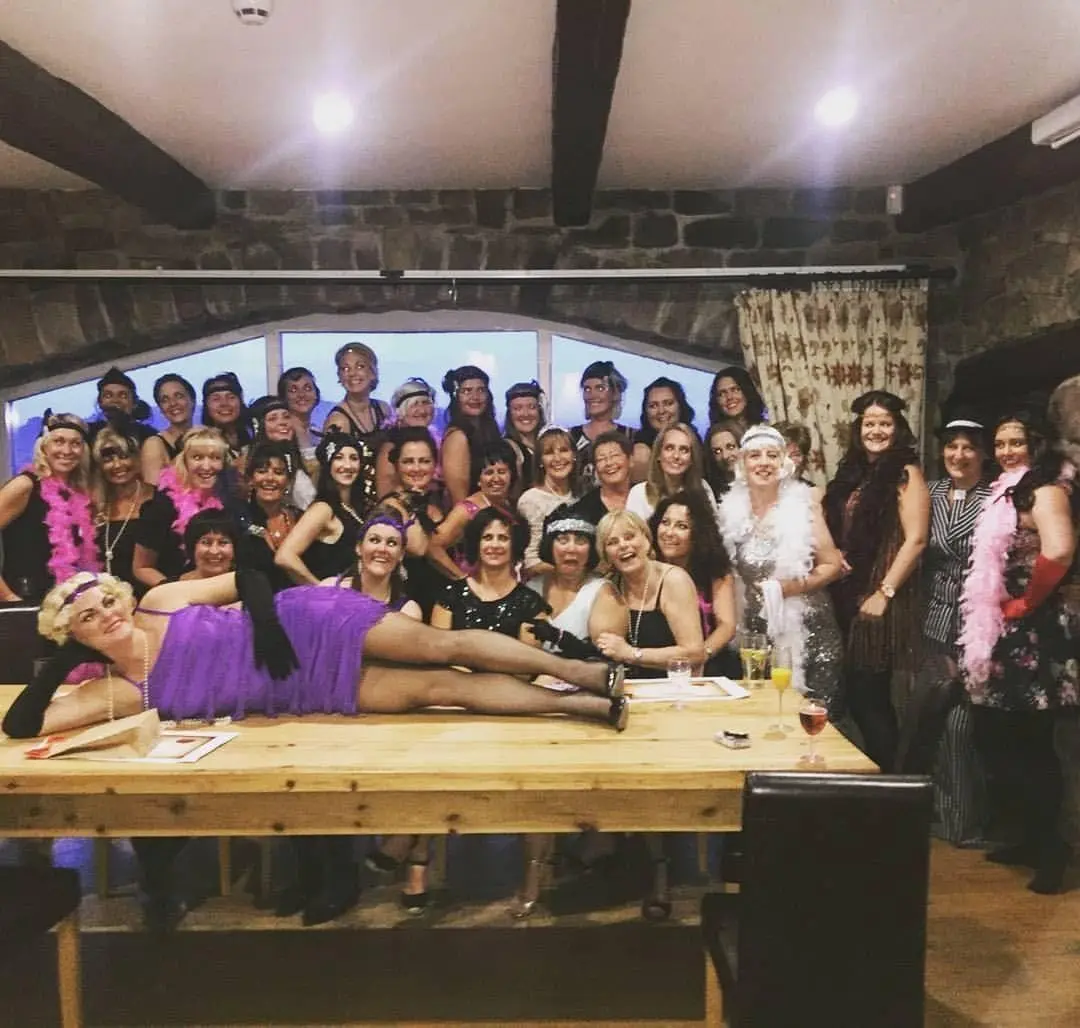 A hen party in costume gathered round a table at their murder mystery