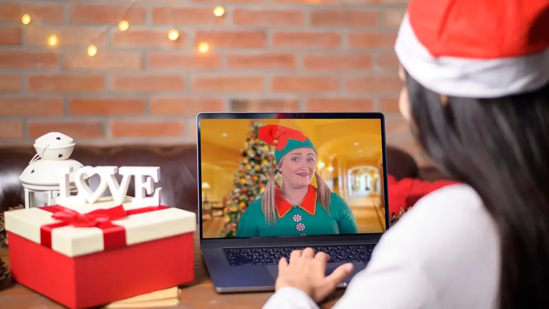 A host dressed as an elf on a laptop screen, beside Christmas presents