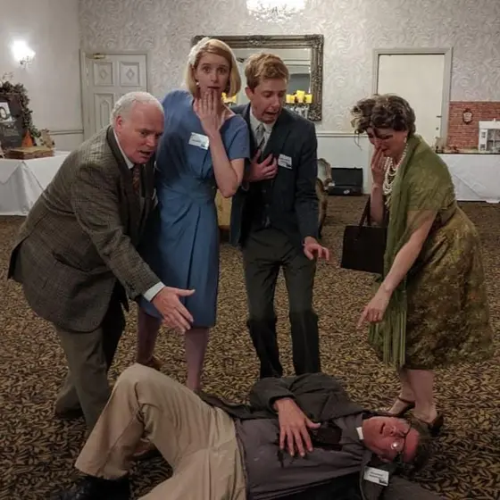 Actors in costume gathered round the victim at a murder mystery