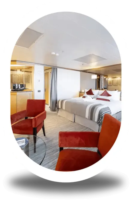 A suite with a double bed and red armchairs in a sitting area